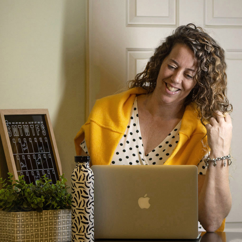 A lady with curly long hair is looking at her laptop and smiling as she reads the about-me section in the sidebar of a blog.