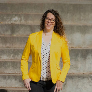 A smiling lady with curly hair and glasses invites potential clients to get in touch with her.