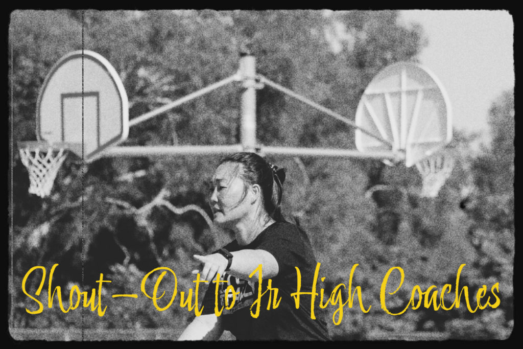 A female junior high school coach is seen in front of two basketball hoops while giving instruction