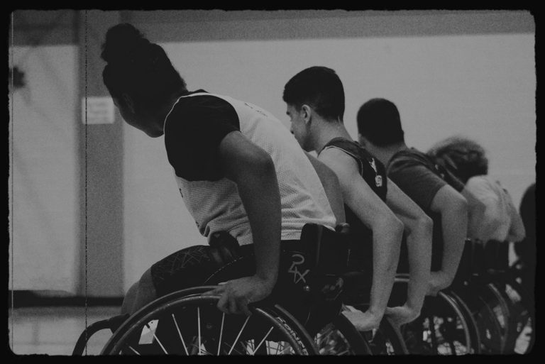 A team of wheelchair basketball players is seen lined up, ready to roll away for a sprint at their basketball practice.